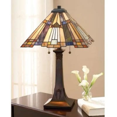 Lampe Tiffany authentique au style Art déco sur socle sombre, abat-jour en vitraux colorés près d'une vase blanche et livres. valeur d'une lampe tiffany authentique.