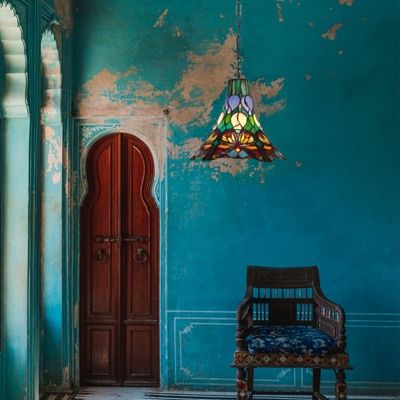 Pièce chambre style tiffany decoration : mur turquoise patiné, porte en bois et lampe Tiffany suspendue au-dessus d’un siège ancien.