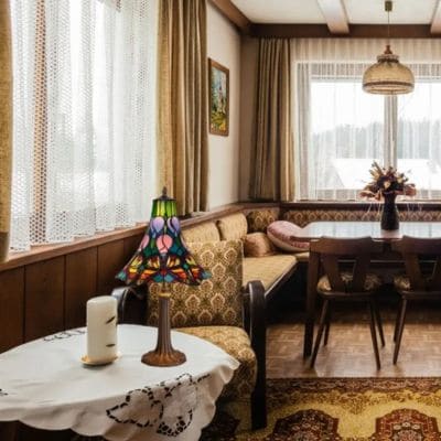 Salon chaleureux avec lampe Tiffany colorée sur table ronde et coin repas en arrière-plan, évoquant l’atmosphère d’une lampe Tiffany authentique.